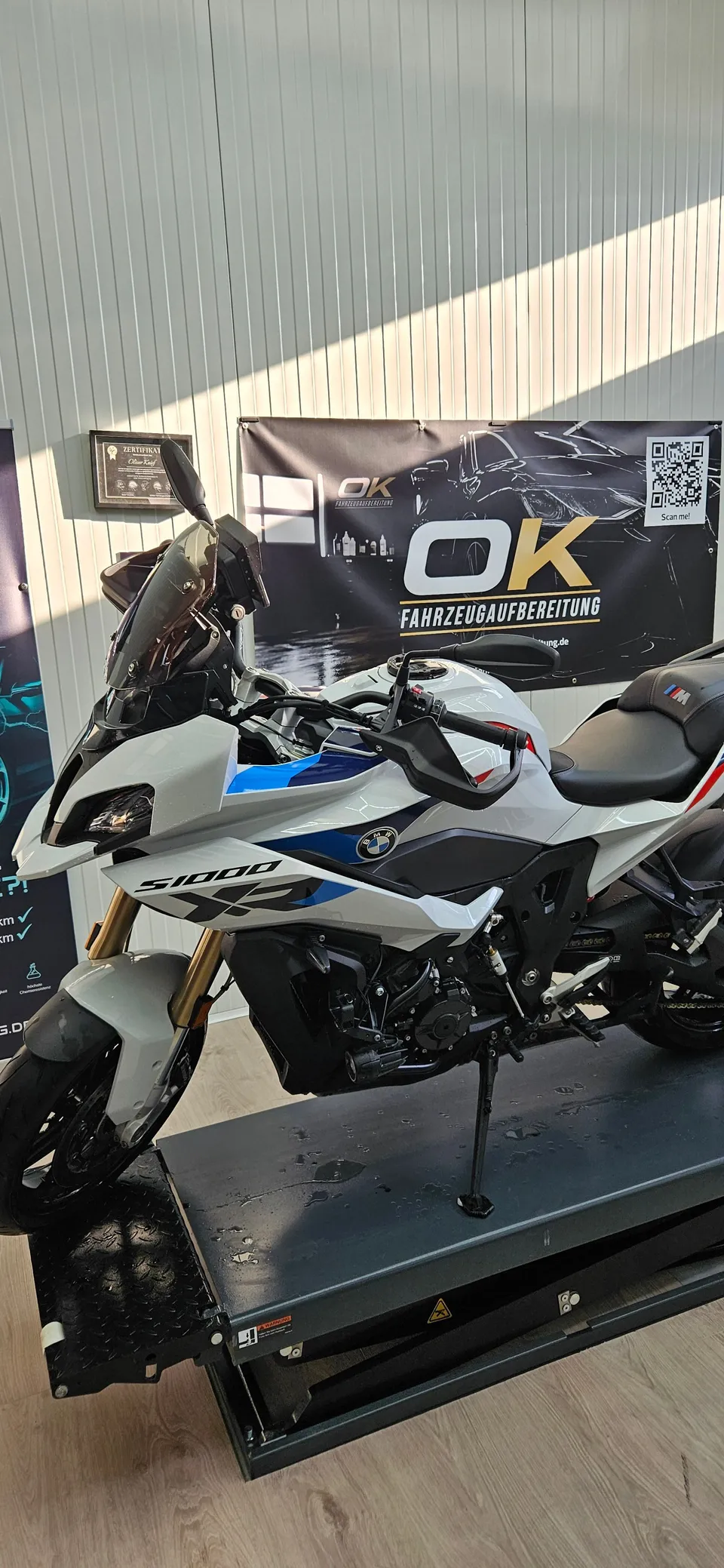 BMW S1000 XR auf der Hebebühne vor dem Firmenbanner von OK Fahrzeugaufbereitung