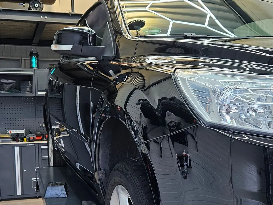 Schwarzes Auto auf der Hebebühne bei OK Fahrzeugaufbereitung: hochglanzpolierter Kotflügel und Scheinwerfer nach der Aufbereitung